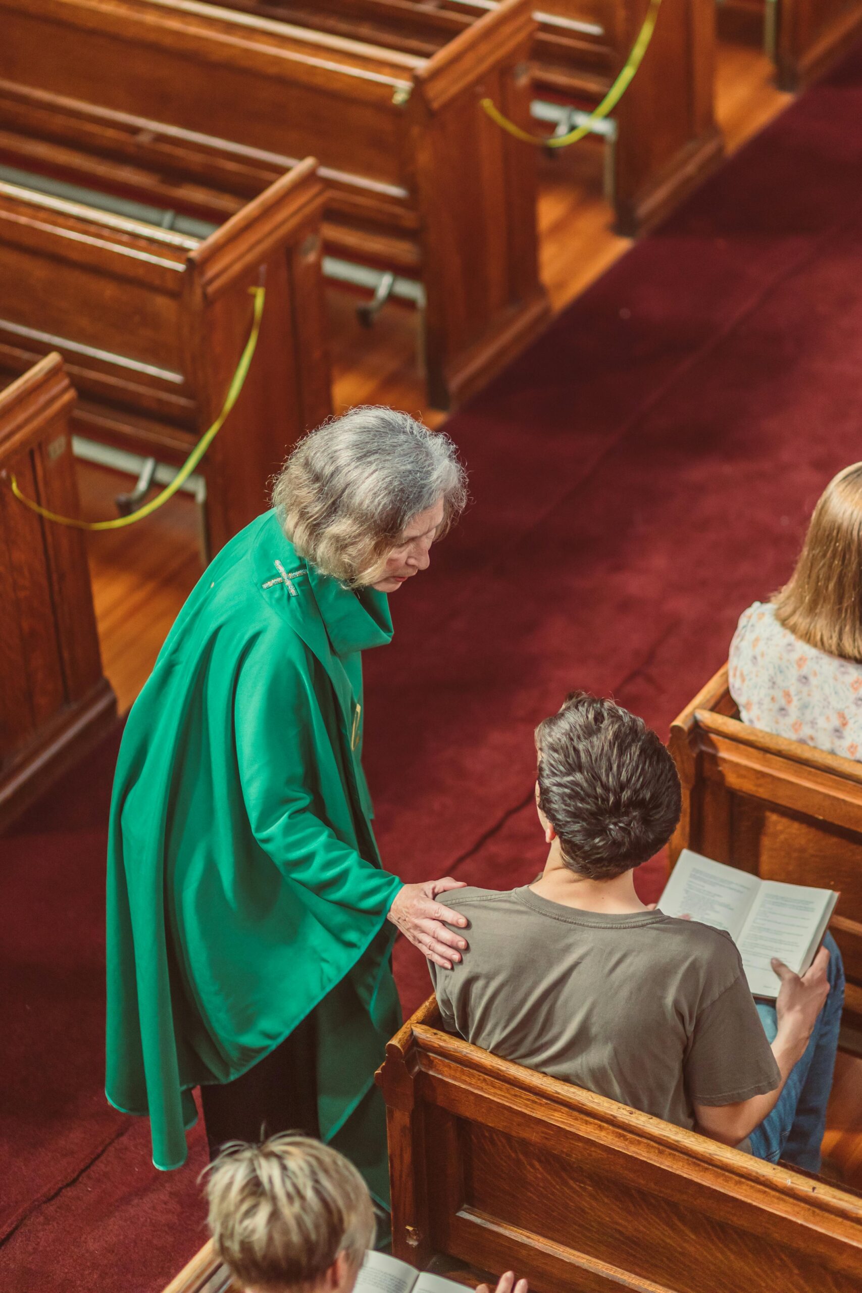 A priest comforts a man in a church pew, fostering a sense of community and faith.